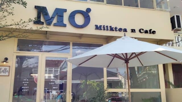 A yellow two-story café in Hoi An with MÓ Milktea n Cafe sign, outdoor seating, and a white umbrella.