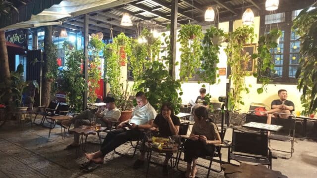 People relaxing at an outdoor café in the evening in Hoi An, surrounded by plants and warm lighting.