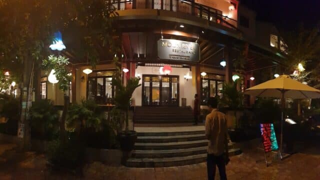 Night view of Moon River Restaurant entrance, glowing with colorful lanterns and a person standing outside.