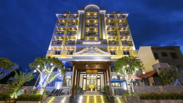 A brightly lit boutique hotel with balconies, glowing at night against a deep blue sky, offers guests access to a luxurious spa.