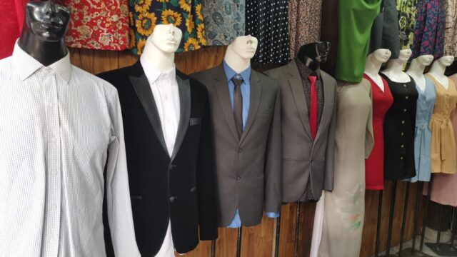 Mannequins dressed in suits and dresses are displayed in front of patterned fabric rolls in a Hoi An boutique.
