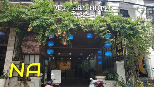 Front entrance of Southern Hotel Hoi An, with blue lanterns, plants, and parked motorbikes.