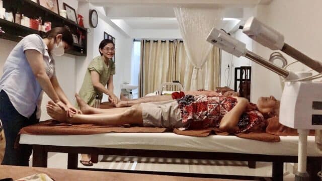 Two women giving a foot massage to a person lying on a spa bed in a treatment room.