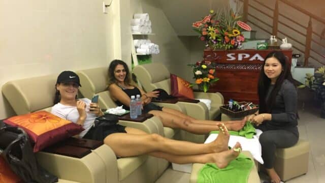 Two women relax in spa chairs getting pedicures while a spa worker helps with their feet.