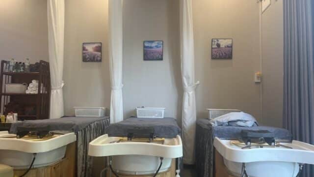 Three spa beds with sinks in front at New Moon Spa, white curtains, and lavender pictures adorn this calm, relaxing room.