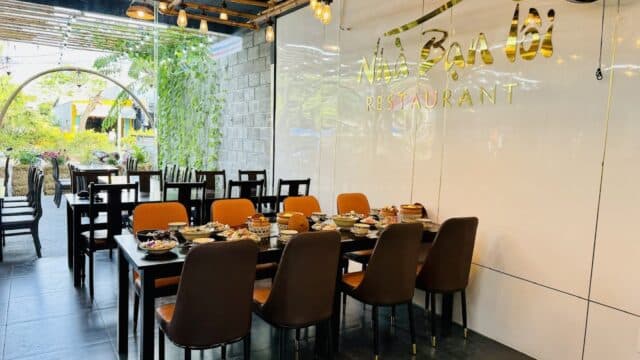 A modern restaurant dining area in Hoi An with a set table, brown chairs, and a wall sign reading NHÀ BẠN 161 RESTAURANT.
