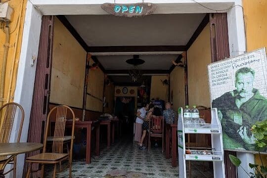 Entrance to a cozy café and restaurant with wooden chairs, yellow walls, and a sign reading Café des Amis - Nhà Hàng - Open.