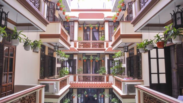 Open-air courtyard at Nhi Nhi Hotel with balconies, potted plants, and decorative railings on multiple floors.