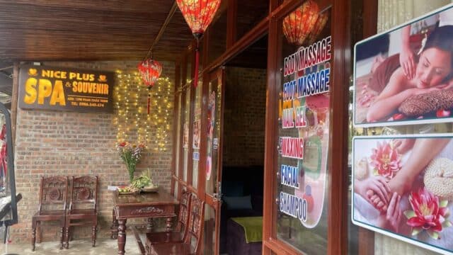 Entrance to Nice Plus Spa with lanterns, fairy lights, wooden chairs, and posters advertising massage services.