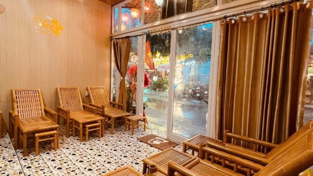 Cozy spa room with bamboo chairs, stone floor, warm lighting, and large windows with brown curtains.
