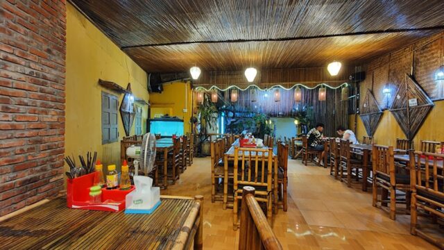 A cozy Old Garden Restaurant with bamboo furniture, warm lighting, and neatly arranged tables, mostly unoccupied.