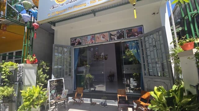The entrance of a beauty spa with open doors, chairs, potted plants, and a sunny exterior.