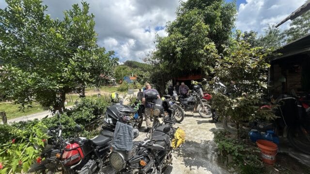 Several motorcycles parked outdoors as people gather, enjoying a partly cloudy day and lush greenery during Onyabike Adventures motorcycle tours in Vietnam.