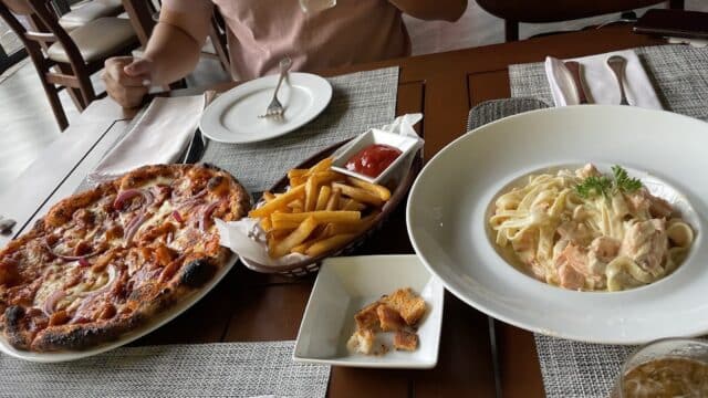 A table at Opal Moon Bistro with pizza, fries with ketchup, pasta, a drink, and a person holding a glass of juice.