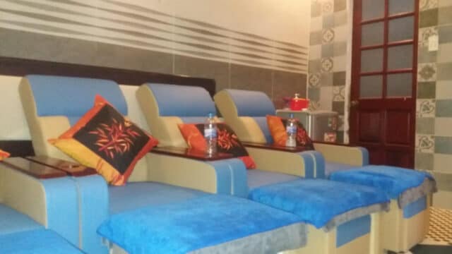 Four blue and beige recliner chairs with colorful pillows and bottled water in the cozy Orange Orange Spa tiled room.
