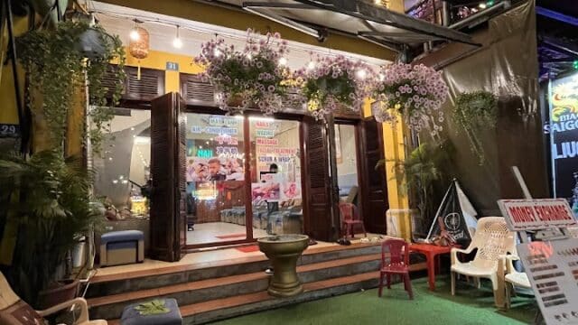 A brightly lit Orange Orange Spa entrance at night, with chairs, towels, hanging flowers, and colorful signs.