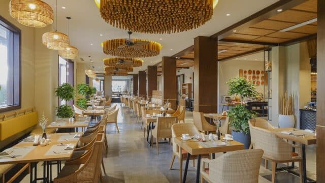 Modern Hoi An restaurant with wooden furniture, large windows, and decorative ceiling lights, set for dining.