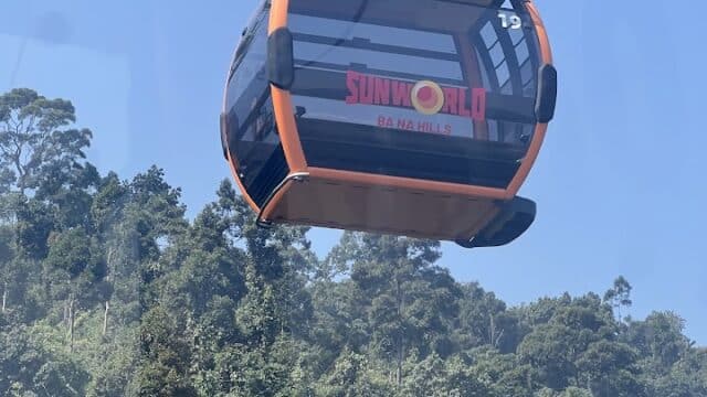 Orange Sun World Ba Na Hills cable car above green forest—perfect for exploring with Passion Scooter or joining scenic Scooter Tours nearby.
