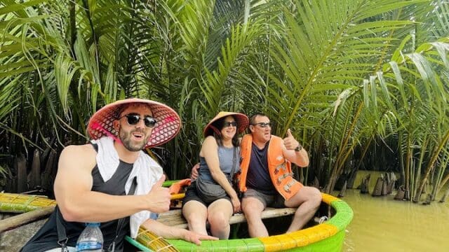 Three people in colorful hats sit in a round green boat on a yellow river—an adventurous outing with Peachy Tours amid lush tropical plants.