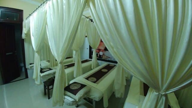 A row of massage beds with white curtains for privacy in a serene Pressure Point Spa room.