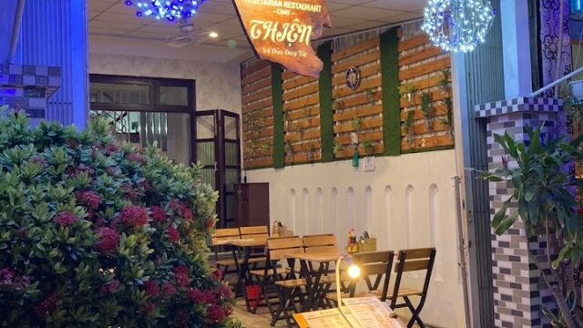 Cozy outdoor vegetarian restaurant, Quán Thiên, with wooden tables, menu stand, hanging lights, and plants at night.