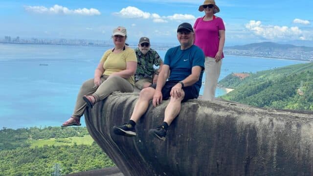 Four people sitting and posing on a large rock with a scenic ocean and city view—an adventure with Quyen Easy Rider in Vietnam.