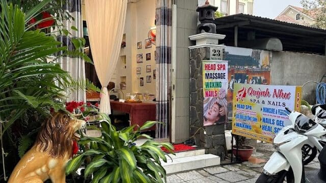 A cozy Quỳnh Như Spa entrance with plants, a lion statue, motorbike parked outside, and spa signs visible.