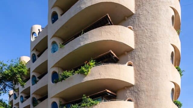 Curved, modern beige Rêu Boutique Hotel with round balconies, circular windows, and plants growing on each floor.