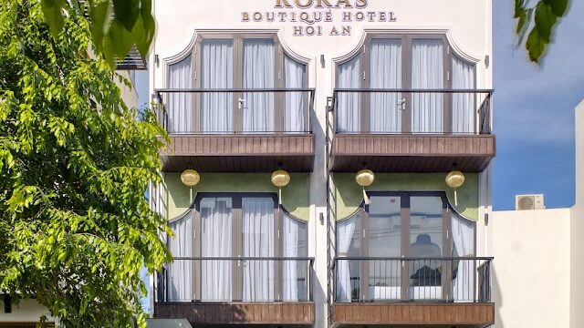 Front view of Rokas Boutique Hotel, with large windows and lush greenery welcoming guests at the entrance.