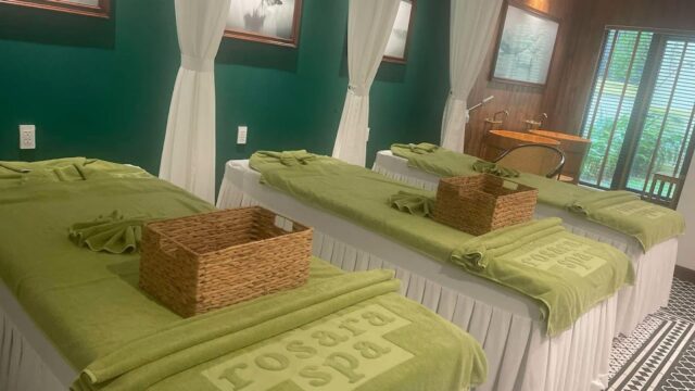 Three spa beds with green towels and wicker baskets in a serene, softly lit treatment room.
