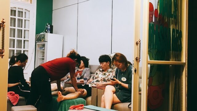 Several people are getting pedicures inside the brightly lit Sea Salt Nails salon at night.