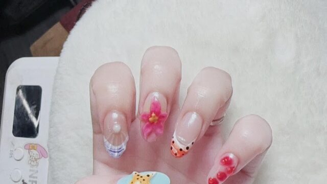 A hand with colorful, playful nail art designs from a Nail Spa, featuring a starfish, flower, hearts, and abstract patterns.
