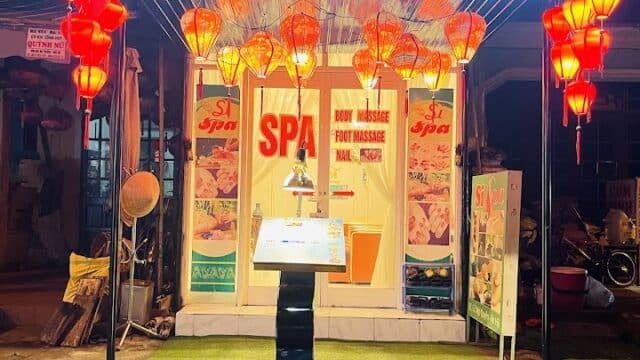 Si Spa storefront at night, brightly lit with red lanterns and a standing sign near the entrance.