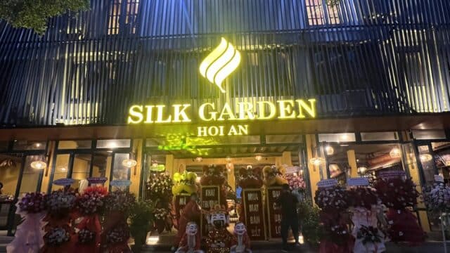 The illuminated Hoi An Silk Garden entrance at night features flower stands and lion dance figures by the doors.