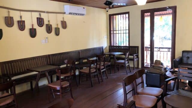 Cozy cafe interior with wooden tables, chairs, wall decor, and sunlight streaming through a door to a balcony.
