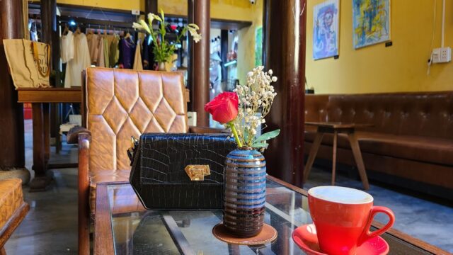 A red coffee cup and a black purse on a glass table in a cozy, Hoi An art-filled café with brown leather chairs.