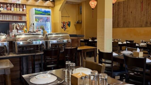 Cozy restaurant with yellow walls, set tables, wooden chairs, and colorful Asian decor accents.