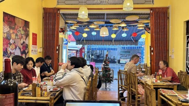 People dining inside Sun Central Restaurant, a cozy, yellow-walled spot decorated with lanterns, a small Christmas tree, and coffee aromas.
