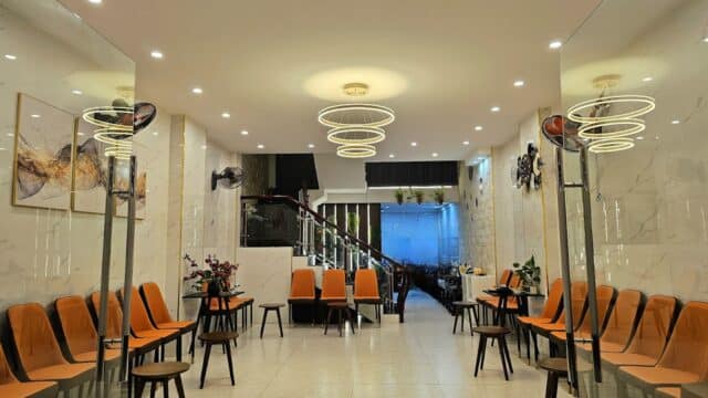 A modern waiting room with orange chairs, small tables, bright lights, and a staircase in the back.