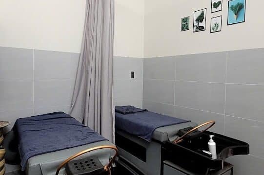 Two massage beds with navy sheets in a spa room, separated by a curtain, with small decor on the wall.