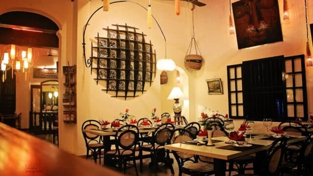Cozy Tam Tam Cafe with elegant table settings, rattan chairs, warm lighting, and decorative wall shelves.