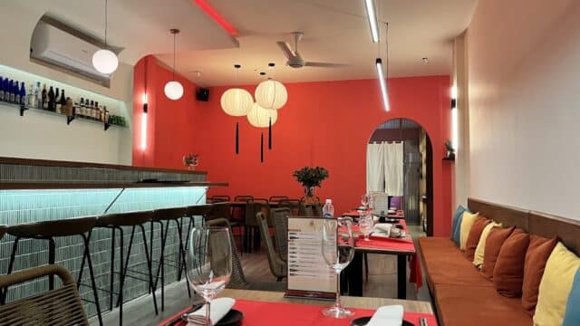 Modern restaurant interior with red and orange walls, hanging lanterns, and colorful cushions—perfect for enjoying sushi or omakase.