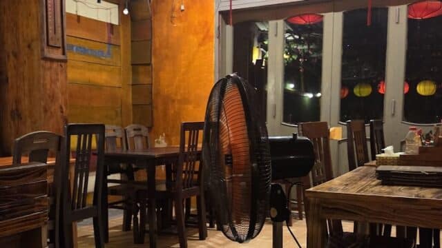 A cozy Thanh Phuong Restaurant interior with wooden furniture, red lanterns, and a standing fan in the center.