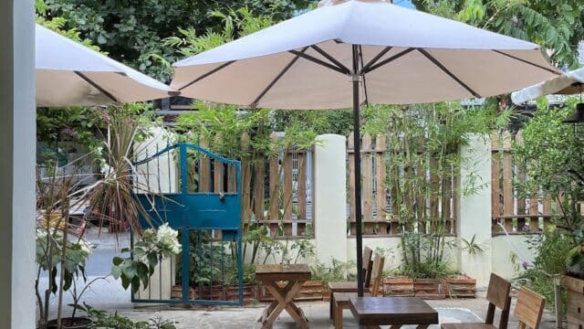 Outdoor patio in Hoi An with wooden tables, chairs, large white umbrellas, greenery, and a wooden fence.