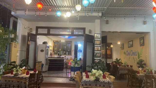 Cozy restaurant interior with colorful Hoi An lanterns, potted plants, and tables set for dining.