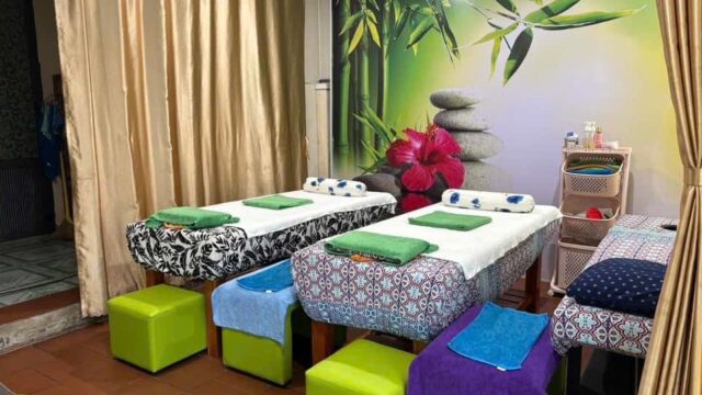 Three massage beds with towels in a beauty spa room, bamboo and stone mural on the wall, stools at each bed at Thuỳ Giang Spa.