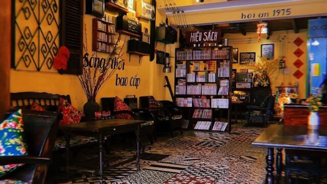 Cozy vintage café in Hoi An with yellow walls, patterned tile floor, bookshelves, and charming antique décor.