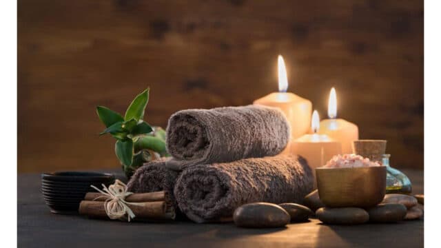 Two rolled towels, candles, stones, and spa massage items arranged on a table for a relaxing atmosphere.