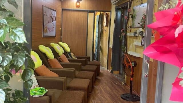 Cozy spa room with brown chairs, soft yellow pillows, wooden floor, plants, and warm hanging lights.