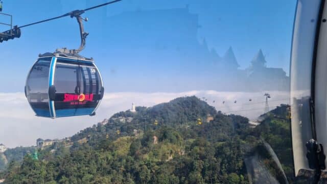 A cable car travels above green hills and forests under a clear blue sky with Tommy Dao Tours.